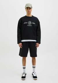 Hanorac negru cu imprimeu "Editie Limitata", asortat cu pantaloni scurți negri, tricou alb, șosete cu dungi și adidași negri cu accente albe.