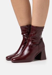 Bottines en fausse cuir bordeaux avec un bout carré et un talon bloc moyen, dotées d'une fermeture éclair et d'un design supérieur froncé pour la texture.