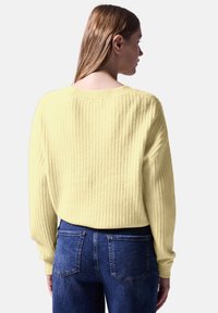 Geel geribbelde trui met lange mouwen, wijde halslijn en een relaxed fit, gecombineerd met donkerblauwe jeans met zakken.