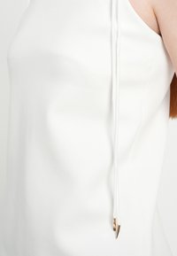 Άσπλο αμάνικο τοπ με απαλό υφή, στρογγυλή λαιμόκοψη και λεπτά κορδόνια με χρυσές μεταλλικές άκρες στη κάθε πλευρά.