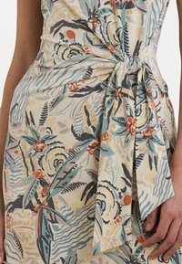 Vestido com padrão floral em bege claro, com detalhes em verde, vermelho e azul. Apresenta um detalhe de nó na frente e uma textura de tecido suave e macia.