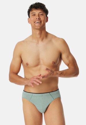 Herrenunterhosen aus hellgrünem Stoff, mit einem schwarzen Bund und kontrastierenden Nähten, in glatter Textur und anliegendem Design.