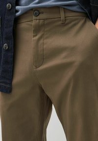 Pantaloni color verde oliva realizzati in tessuto liscio, dotati di una tasca frontale, chiusura con bottone e design slim-fit.