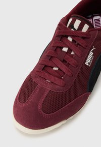 Burgundske tenisice s mrežastim i antilop materijalima, s crnim detaljima, dizajnom na vezivanje i teksturiranim bijelim potplatom. PUMA brendiranje vidljivo.