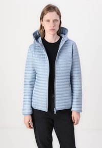 Lichtblauwe gewatteerde jas met een capuchon, voorzien van een rits aan de voorkant, horizontale stiksels en een gladde, glanzende textuur. Zwarte top en jeans eronder gedragen.