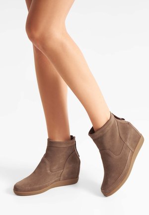 Brown suede ankle boots with a wedge heel, featuring curved seams and a rounded toe, designed for comfort and ease of wear.