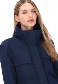 Marineblå, struktureret jakke med høj krave, med to forlommer og glat stoftekstur.