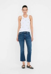 Wit tanktop met kleine geborduurde ontwerpen, gecombineerd met blauwdenim jeans met een mid-rise en zwarte platte schoenen. Gladde stof en rechte pijp.
