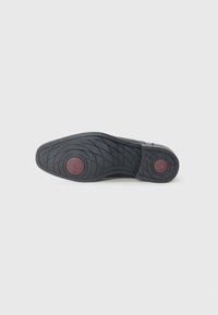 Black rubber shoe sole with a textured surface and circular red accent. Features a zigzag tread pattern for grip and durability.