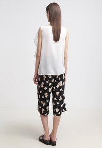 Haut blanc sans manches avec un design superposé ; associé à des culottes noires à imprimé floral et des sandales noires. Tissu lisse, coupe décontractée.