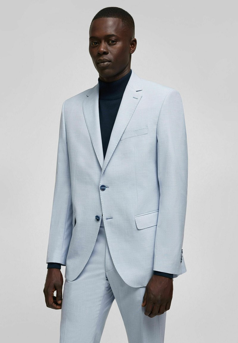 Hellblaues Sakkos mit strukturiertem Design, mit Reverskragen, zwei Knöpfen und Seitentaschen. Über einem navyblauen Rollkragenpullover getragen.