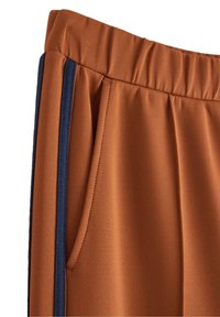 Pantaloni con elastico marrone in vita, dotati di tasche laterali e strisce verticali blu scuro lungo le cuciture esterne.
