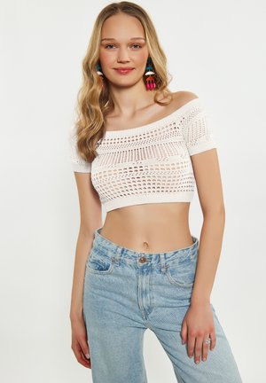 Weißes, schulterfreies Crop-Top mit einem gestrickten, offenen Design. Kombiniert mit hoch taillierten, hellblauen Jeans.