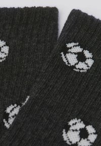 Grå, stickade strumpor med en upprepande vit grafik av en jordglob och pilar. Texturen är ribbad och mjuk, vilket ger en mysig känsla.