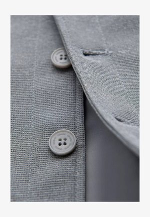 Grijze textuur blazer stof met een close-up van een ronde grijze knop met vier gaten. Glad binnenvoering zichtbaar.