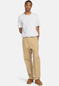 Lysegrå kortærmet t-shirt med brystlomme, parret med beige løstsiddende bukser og brune ruskinds mokkasiner.