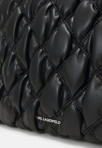 Bolso de cuero negro acolchado con secciones elevadas y suaves y costuras sutiles. Logo "KARL LAGERFELD" en blanco en la parte inferior.