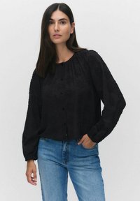 Svart långärmad blus med texturerat blommönster, rund halsringning och knäppning framtill. Kombinerad med ljusblå denim skinny jeans.