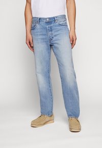 Jeans in denim blu chiaro con vestibilità rilassata, dotati di tasche frontali, leggera scoloritura e lievi abrasioni vicino al ginocchio.