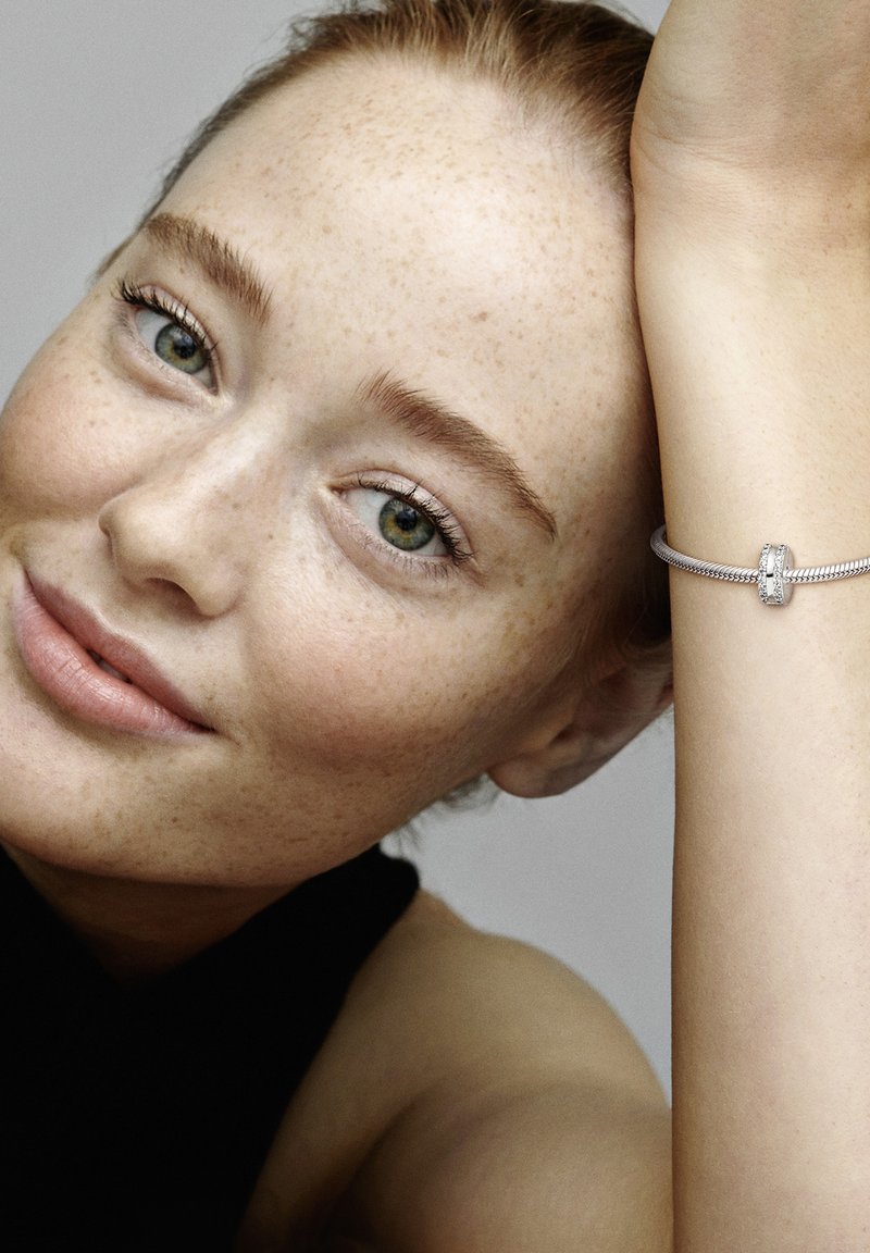 Pulsera de plata con un intrincado diseño trenzado y un cierre decorativo central. La modelo lleva una blusa negra, mostrando la pulsera en su muñeca.