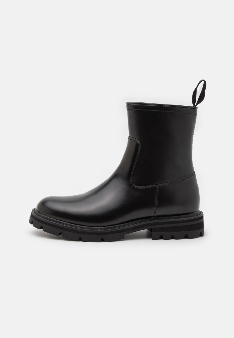 Bottine en cuir noir avec semelle crantée épaisse et languette à l'arrière, vue de profil sur fond blanc.