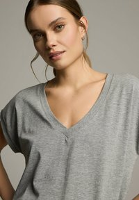 Szary t-shirt z dekoltem w serek, z krótkimi rękawami, wykonany z miękkiego materiału. Charakteryzuje się luźnym krojem i subtelnym przeszyciem wzdłuż dekoltu.