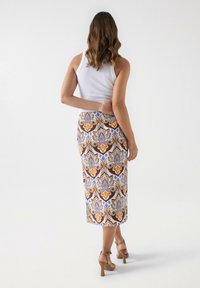 Falda midi con estampado que presenta un diseño floral en tonos marrones, azules y naranjas, combinada con una camiseta ajustada blanca y sandalias de tacón marrones.