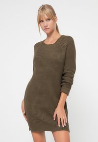 Πλεκτό ελαστικό φόρεμα σε ελιόχρωμο με στρογγυλή λαιμόκοψη, ριγωτή υφή, μακριά μανίκια και πλαϊνές σχισμές, εφαρμοστή σιλουέτα.