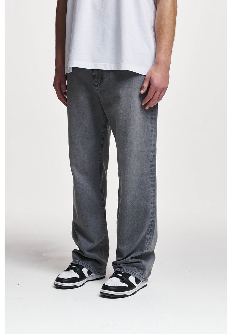 Jeans de mezclilla gris con corte relajado, que presentan un acabado descolorido, costuras visibles y pierna recta, combinados con zapatillas en blanco y negro.