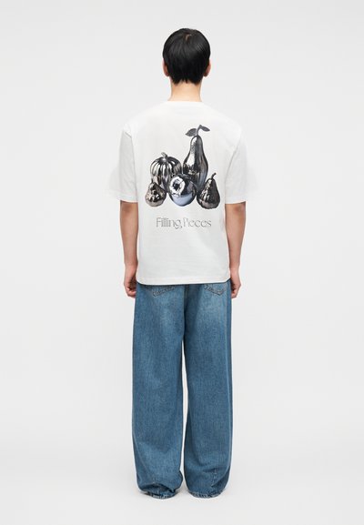 Λευκό βαμβακερό t-shirt με γραφικό διάφορων φρούτων στην πλάτη και το κείμενο «Filling Pieces» κάτω από το σχέδιο. Χαλαρή εφαρμογή, κοντά μανίκια.