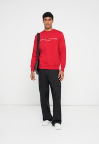 Felpa rossa con logo bianco, scollo a girocollo e polsini a costine. Abbinata a pantaloni cargo neri e sneakers bianche. Outfits casual, design funzionale.