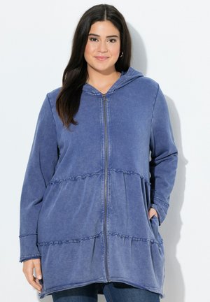 Blue zip-up hoodie in soft fabric, featuring a ruffled hem, pockets, and a hood. Smooth texture with a relaxed fit.