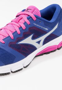 Chaussure de sport bleue avec des accents roses. Comprend un matériau en maille, des superpositions texturées et une semelle blanche avec des éléments de traction noirs.