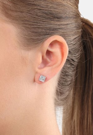 Orecchino a perno quadrato in argento con un brillante zirconia cubica trasparente al centro, posizionato sull'orecchio di una persona con capelli castano chiaro.