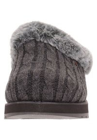 Pantofole grigie lavorate a maglia con motivo a treccia, colletto in pelliccia sintetica e suola piatta in gomma. Superficie testurizzata con una finitura morbida.