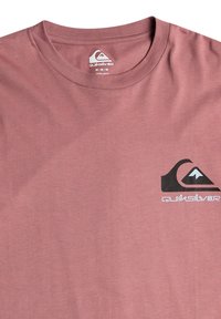 Rosa bomull t-shirt med korta ärmar, rund hals och en svart Quiksilver-logotyp på vänster bröst, med en mjuk textur.