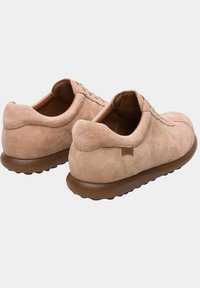 Beige suede sneakers with a rounded shape, lace-up front, and textured rubber soles. Features a brown accent on the heel.