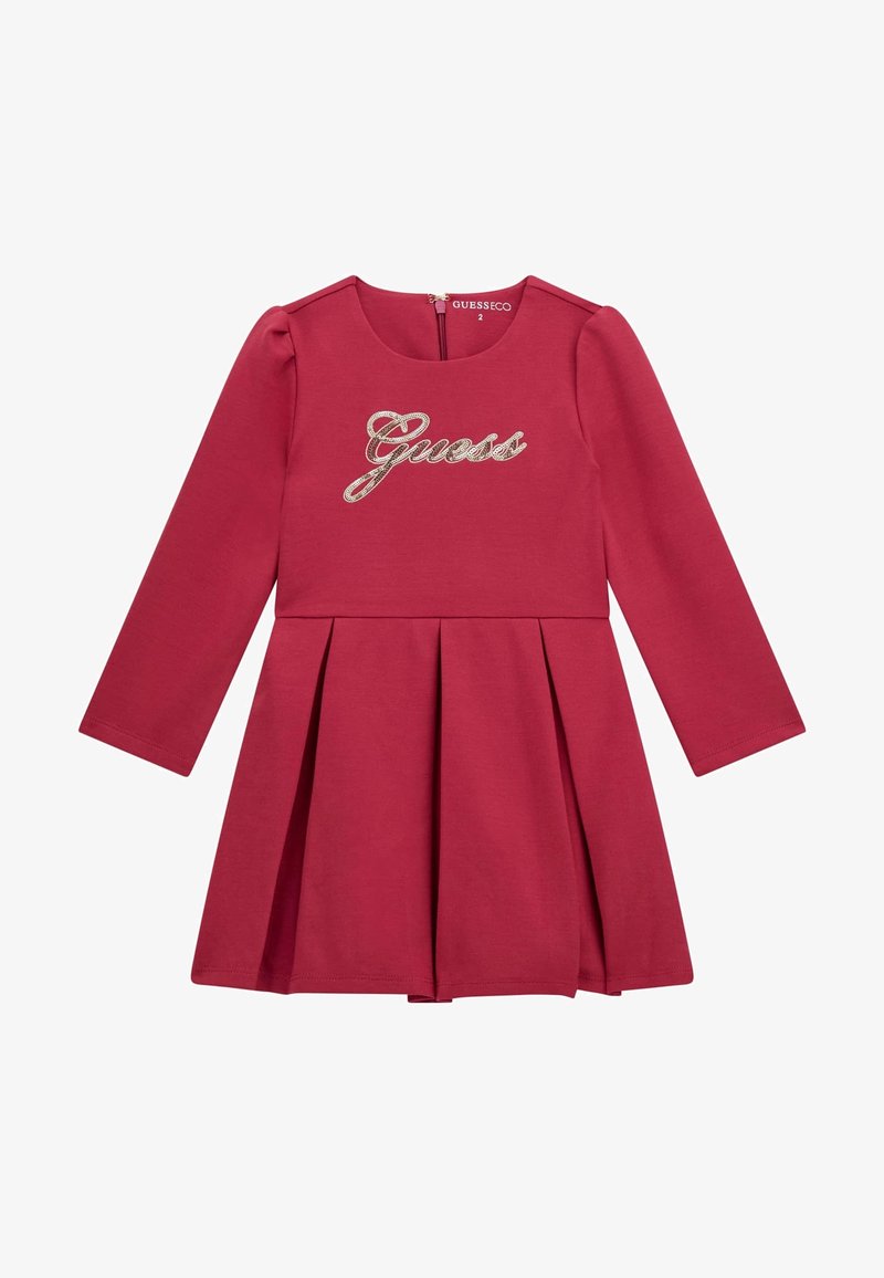 Robe en coton rouge à manches longues avec une jupe plissée, présentant un logo "Guess" pailleté sur la poitrine et une fermeture éclair dans le dos.