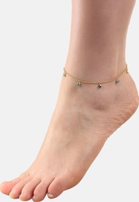 Tobillera con cadena de oro que presenta pequeñas cuentas azules redondas. La cadena tiene un diseño delicado, envolviendo el tobillo. Se ve un pie de tono de piel.