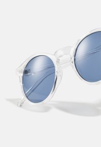 Lunettes de soleil rondes avec monture en plastique transparent et verres teintés en bleu, présentant des surfaces lisses et des branches légèrement courbées.