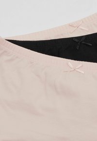 Deux camisoles : une rose clair et une noire. Les deux sont en tissu doux avec des bretelles fines, et présentent de petits accents en ruban au niveau du col.