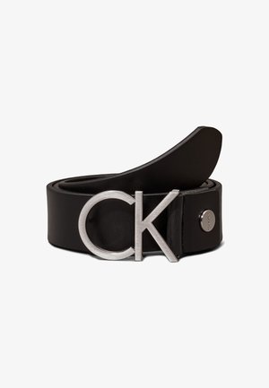 Czarny skórzany pasek zwinięty z dużą srebrną klamrą "CK" i metalowym guzikiem z wytłaczanym tekstem.