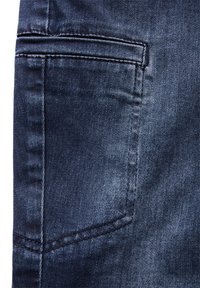 Tissu en denim bleu foncé, avec une poche arrière dotée de coutures visibles. Texture lisse avec un léger effet de décoloration autour de la zone de la poche.