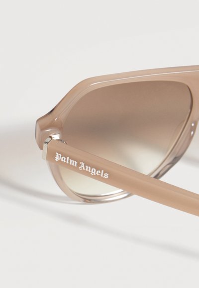 Lunettes de soleil teintées beige avec verres dégradés et logo "Palm Angels" sur la branche, présentées sur fond blanc.