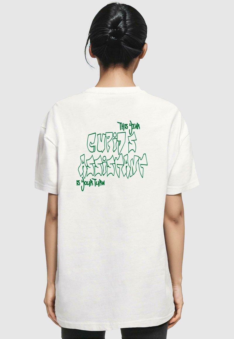 Weißes, übergroßes T-Shirt mit kurzen Ärmeln. Grafischer Text auf der Rückseite: "Diese Liebevolle Cuppids Assistentin ist an der Reihe" in grüner, stilisierter Schrift.