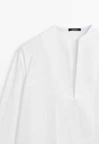 Blouse blanche à manches longues avec un décolleté en forme d'encoche en V et une étiquette portant la mention « Massimo Dutti Made in Portugal ».