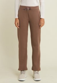 Joggers in tessuto morbido e marrone con cintura elastica regolabile, tasche laterali e una vestibilità comoda, abbinati a scarpe chiare.