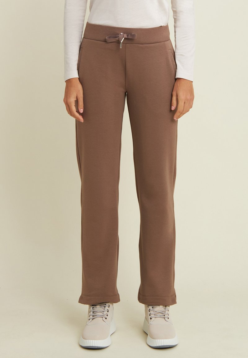 Joggers in tessuto morbido e marrone con cintura elastica regolabile, tasche laterali e una vestibilità comoda, abbinati a scarpe chiare.