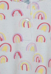 Weißer Stoff mit bunten Regenbogenmustern in Rot, Gelb, Lila und Pink, mit einem Nahaufnahme von einem Druckknopfverschluss.