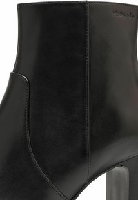 Bottine en cuir noir avec un bout arrondi, texture lisse, talon bloc haut et détails de couture discrets.